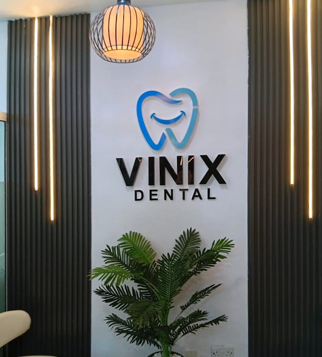 The Vinix Dental logo on the waiting area wall, between lit black slatted panels, with a pendant lamp, a potted palm and cream chairs