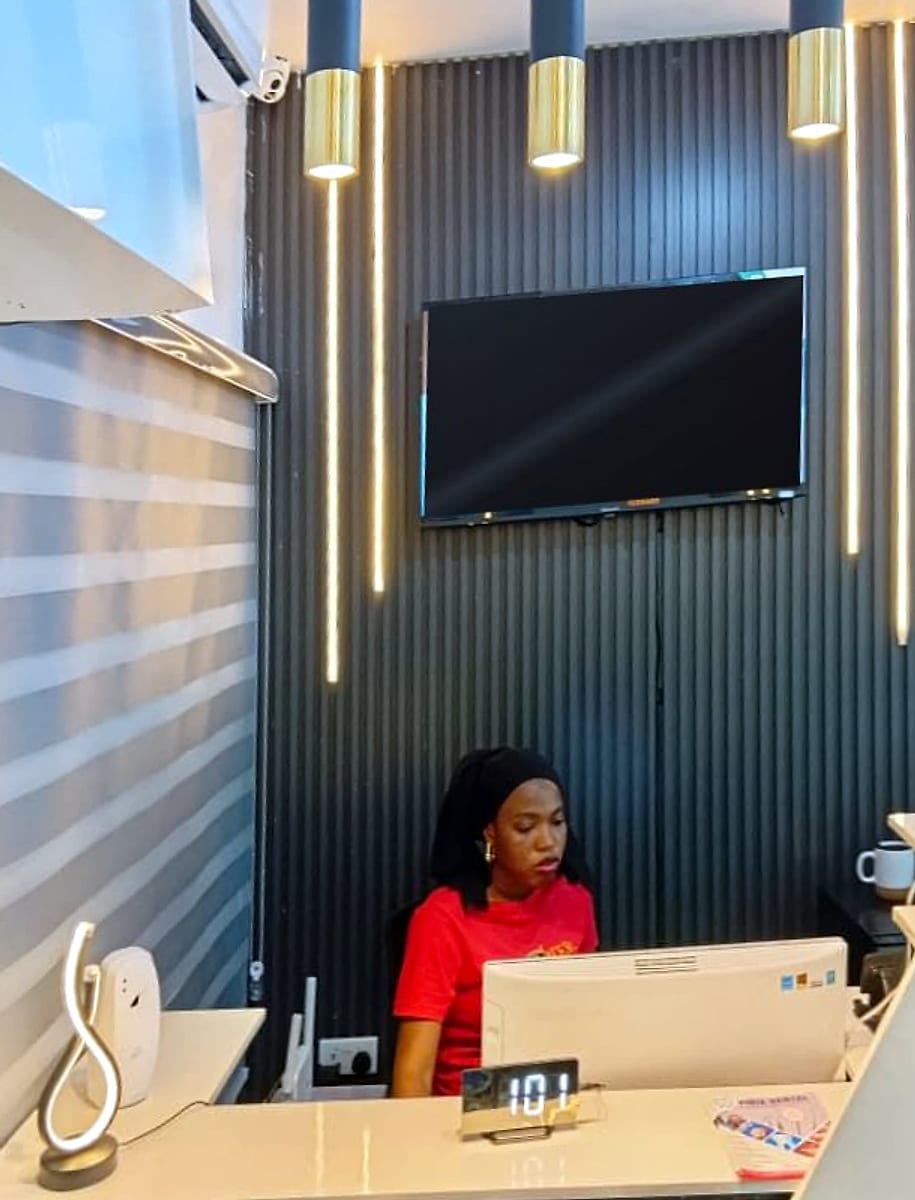The Vinix Dental reception desk, with a receptionist at the computer in front of a black slatted wall lit by gold pendant lamps and vertical light strips